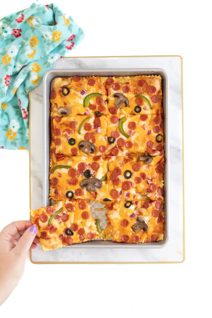 woman's hand grabbing a slice of pizza from a baking sheet