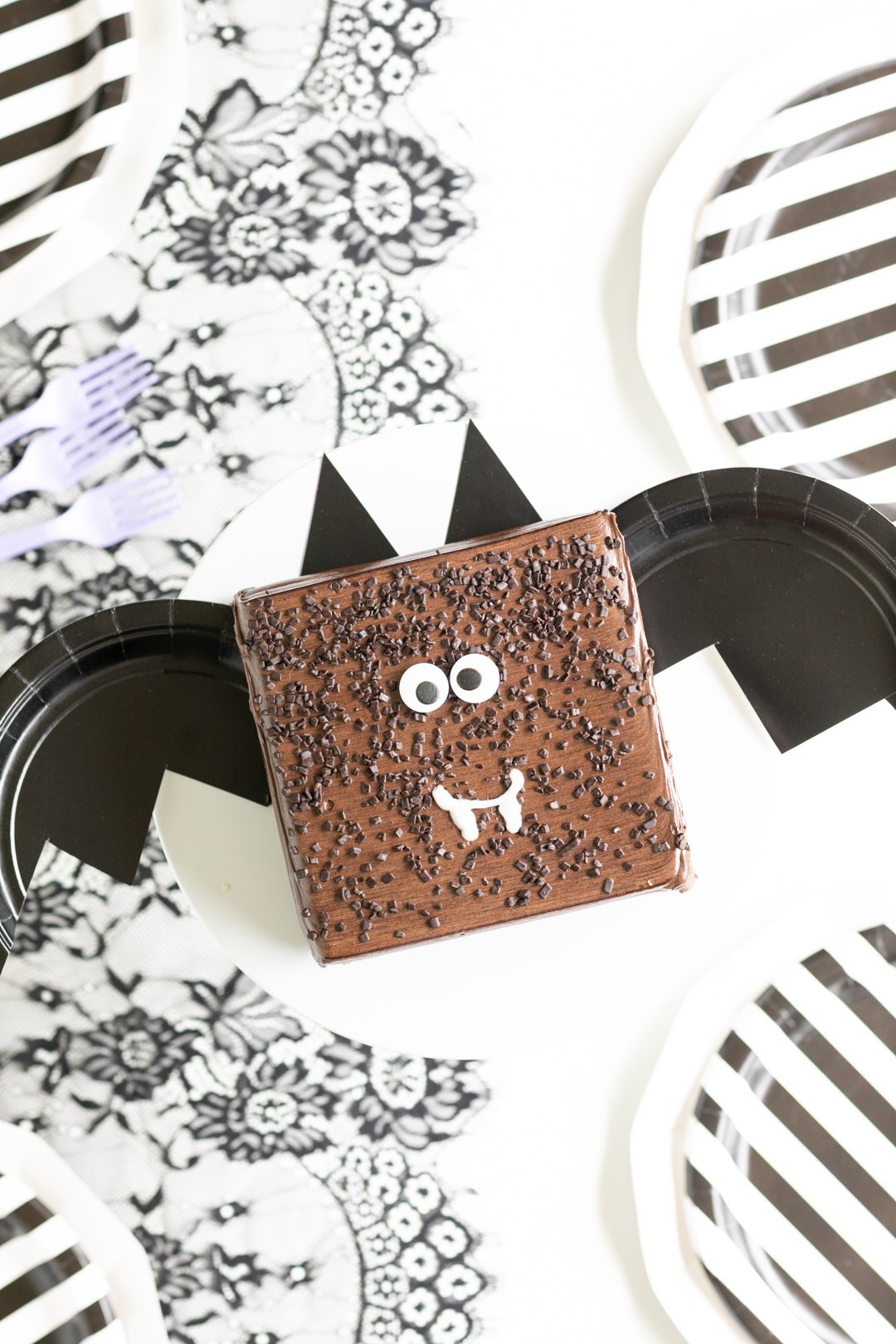 spooky party table with small diy bat cake using black paper plates. Black and white striped paper plates and black lace runner.