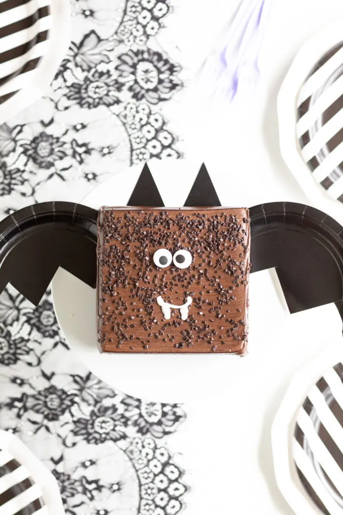 square chocolate cake transformed into a bat cake with paper plate bat wings and ears and large candy eyes and icing fangs.