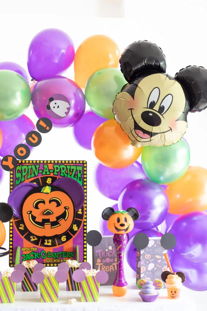 disney inspired halloween party table at home with mickey mouse balloons, colorful balloon arch, games, treat bags and mickey mouse halloween foods