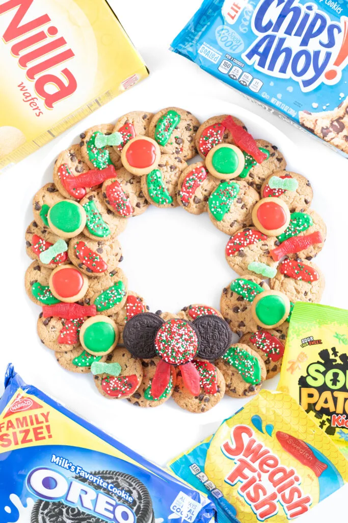 christmas cookie wreath made with chips ahoy, oreo, nilla wafters, swedish fish and sour patch kids. packages of products are surrounding the cookie wreath on the table.