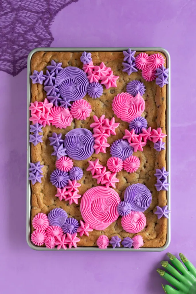 beginning stages of frosting a sheet pan cookie using pink and purple buttercream decorations using a french tip and open star tip.