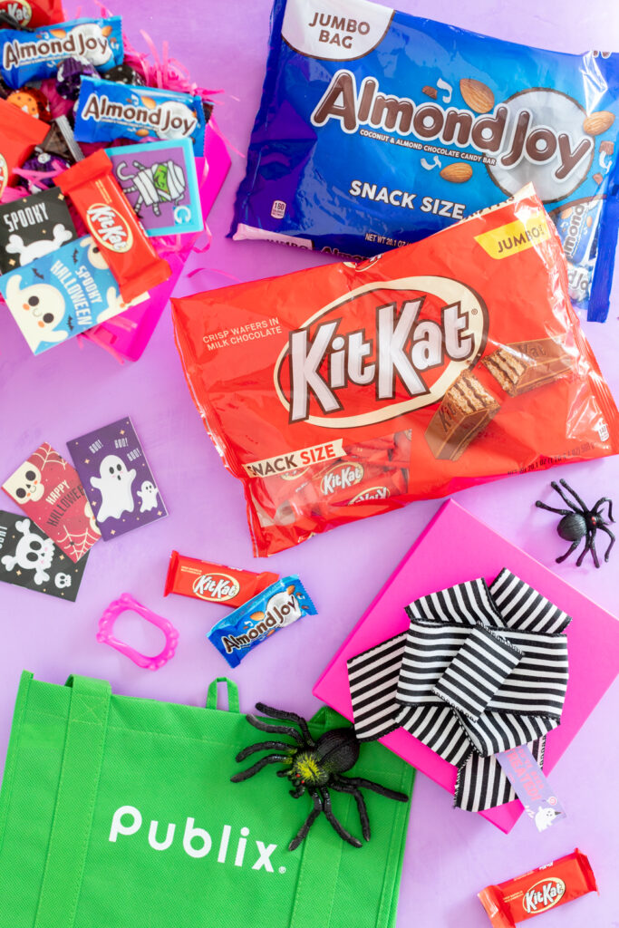 bags of halloween candy kit kat and almond joy, publix reusable shopping bag and halloween treats, pink gift box with striped ribbon on top
