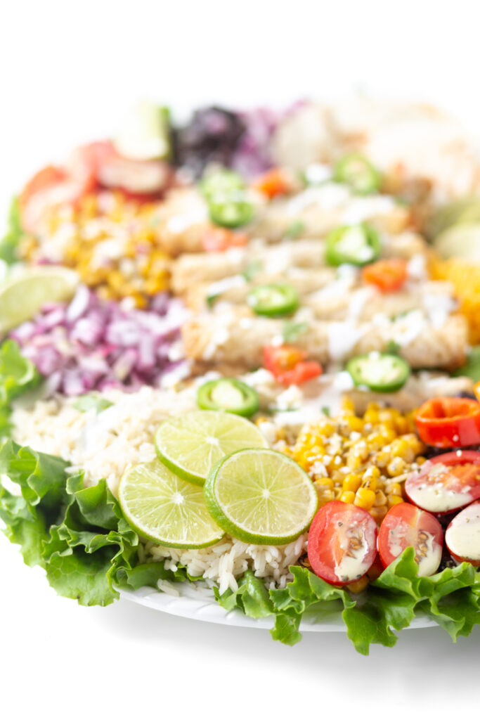 angled down shot of a big mexican dinner board with slime slices, grape tomatoes with dressing drizzled on top, roasted corn, jalapenos.