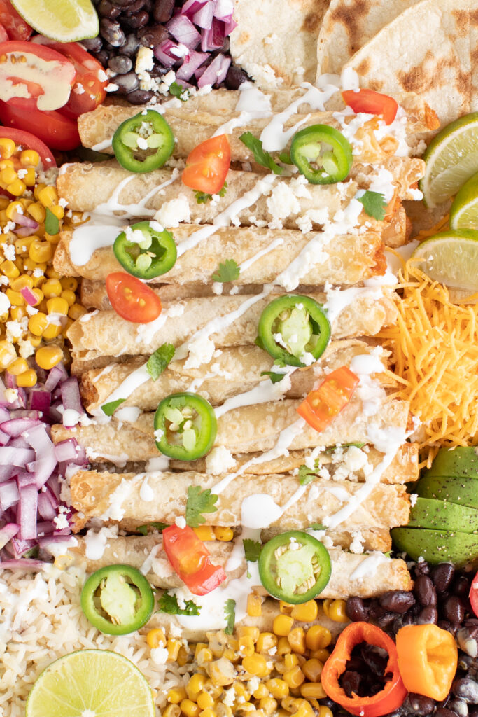 close up shot of taquitos with sliced jalapeno, chopped grape tomatoes and table cream drizzled on top.