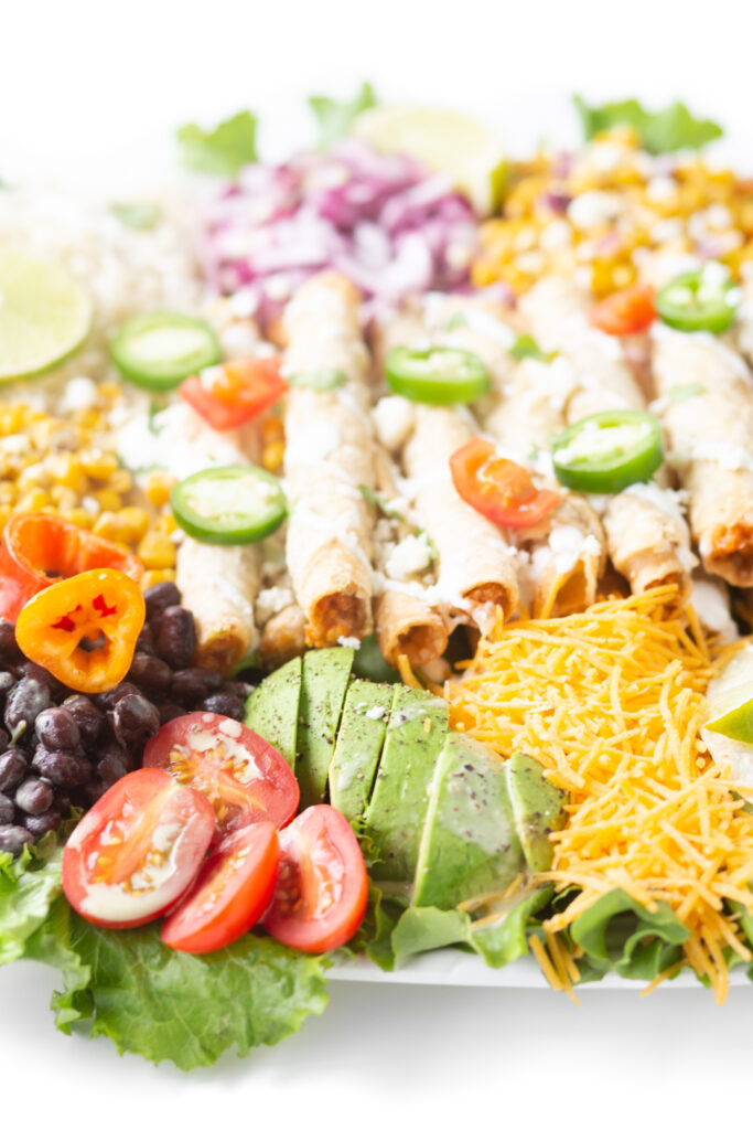 up close view of stack of taquitos resting on a bed of mexican inspired ingredients.