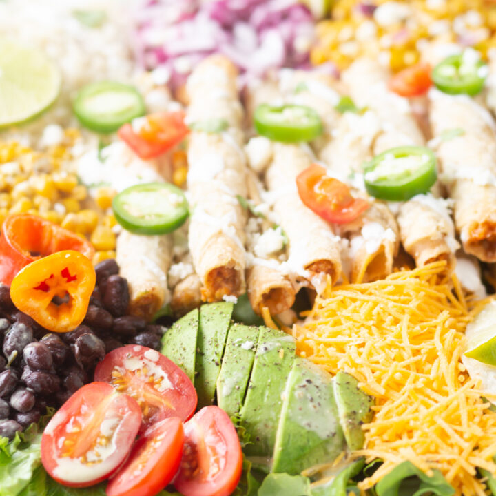 up close view of stack of taquitos resting on a bed of mexican inspired ingredients.