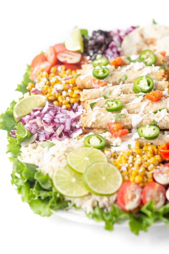 angled down shot of huge mexican dinner platter with taquitos and all the fixings. jalapeno and lime slice garnishes.