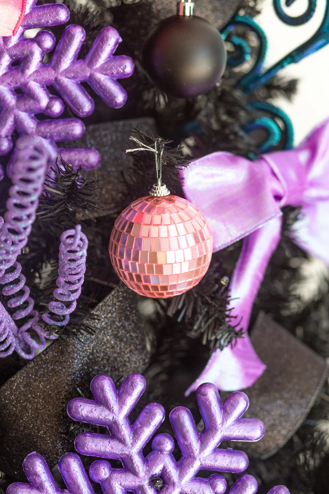 up close bubblegum pink colored disco ball styled ornament on a black christmas tree