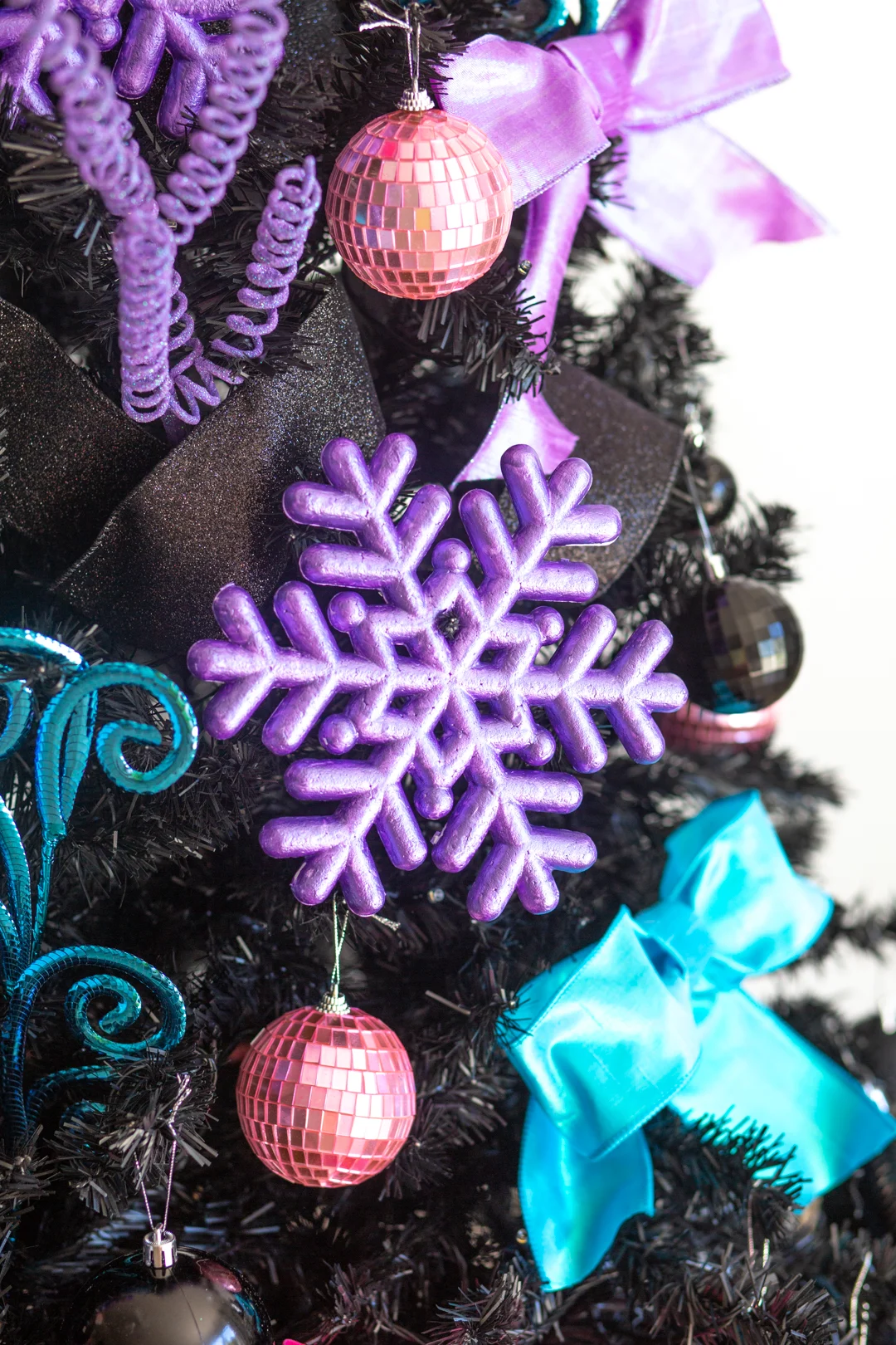 up close view of a styrofoam snowflake painted with metallic purple paint and hanging on a black christmas tree