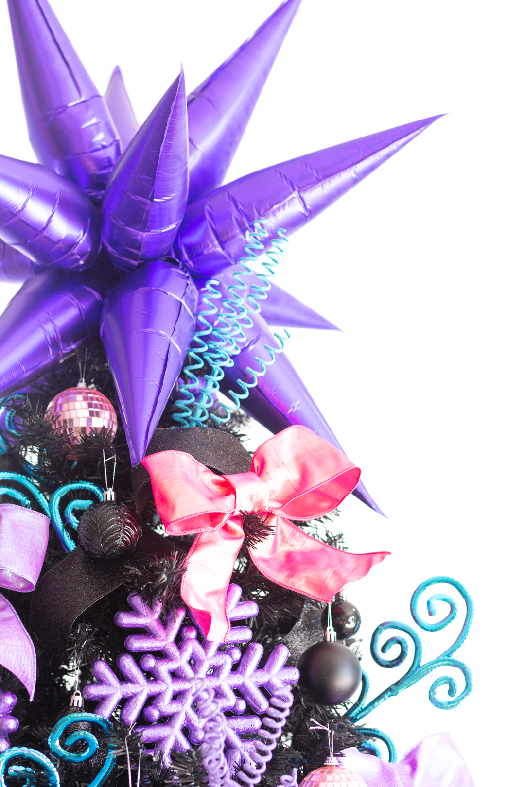 up close of the top of black christmas tree with a metallic purple colored multi point star balloon