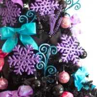 up close view of the center of a black christmas tree to showcase the metallic purple snowflake ornaments, swirly blue floral picks and jumbo zied purple and blue bows.