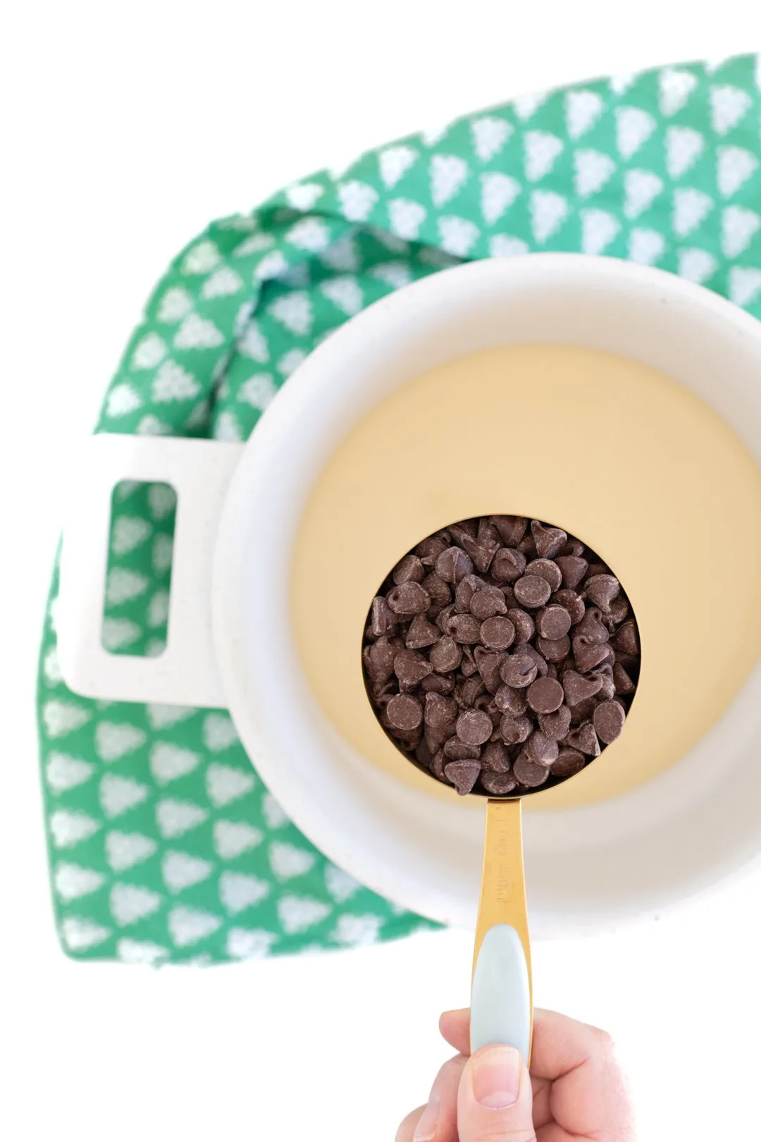 woman holding 1 cup of semi sweet chocolate chips over pan of condensed milk