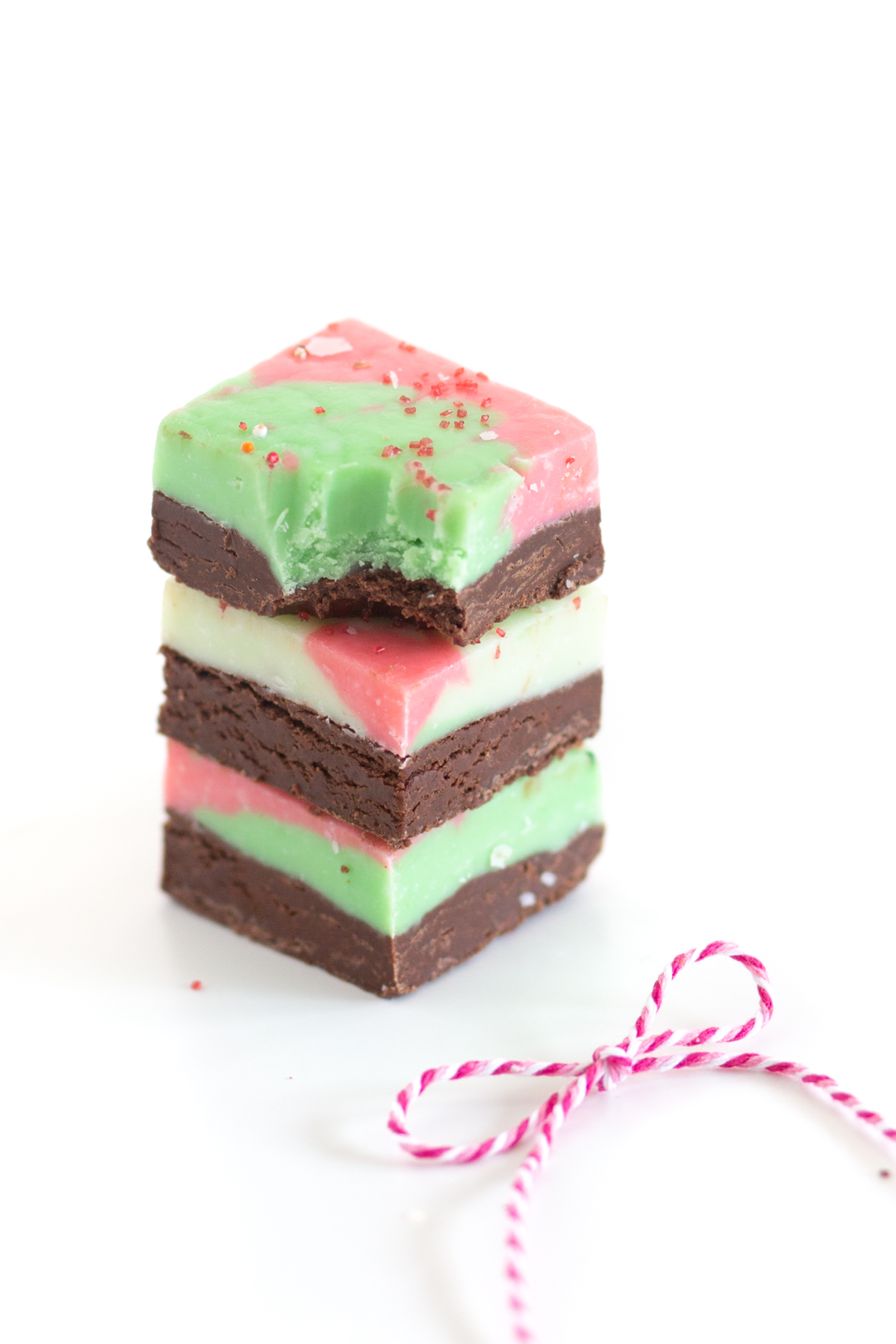 stack of two-layer christmas themed fudge. bottom layer brown chocolate, top layer white chocolate with red and green food coloring swirls, topped with sprinkles.