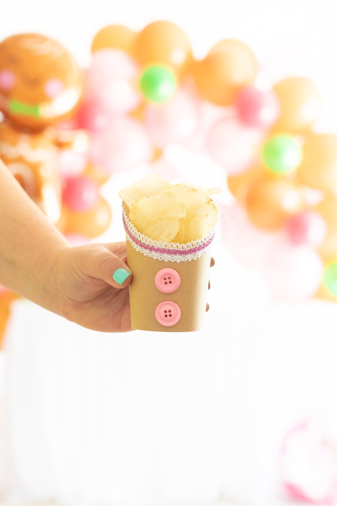 snack cups decorated to resemble gingerbread houses with ribbon trim and pink buttons and filled with potato chip snacks