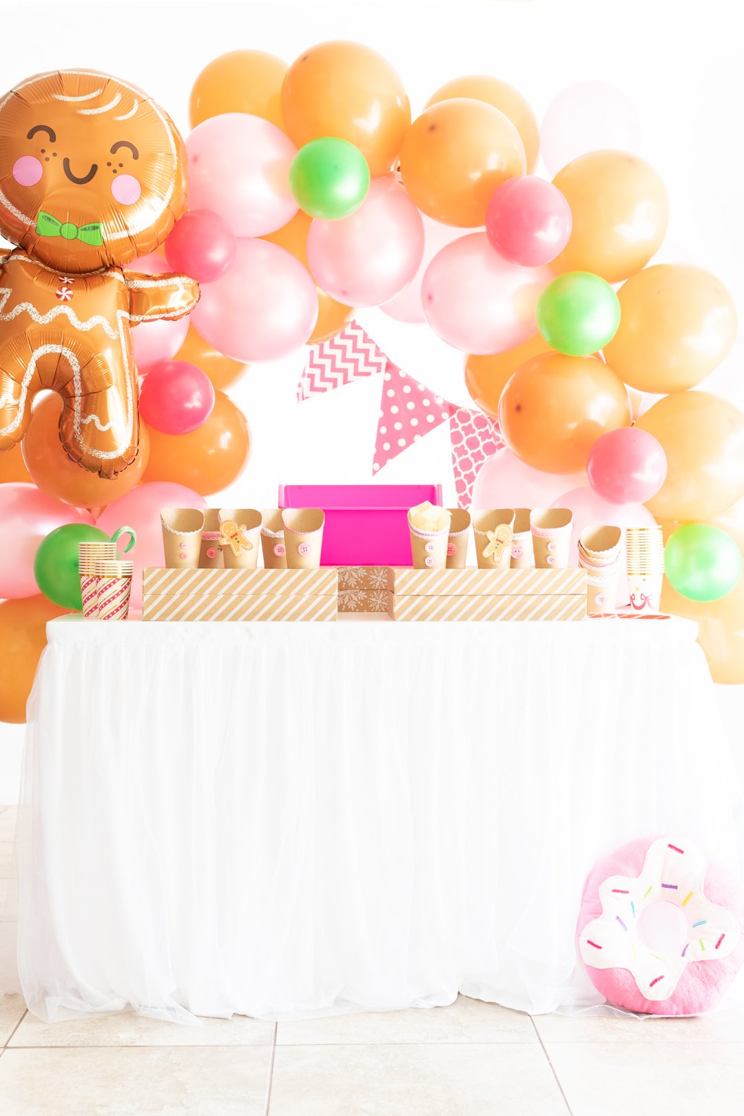 setting up for a gingerbread house themed snack bar. gingerbread inspired snack cups lined up on top of kraft gift boxes with white stripes for serving. Small pink tub set up to hold ice and cans of soda