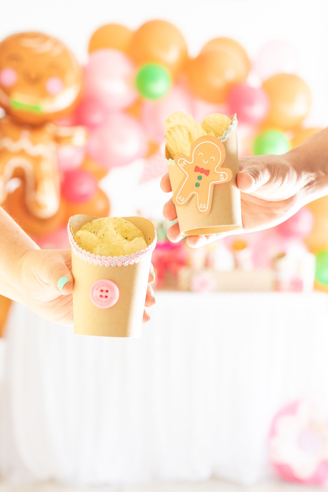 man and woman each holding a gingerbread house themed and decorated snack cup filled with potato chips