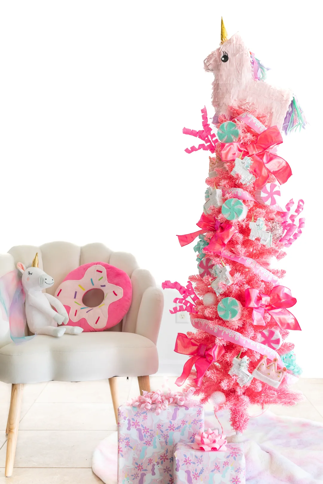 pink unicorn themed christmas tree, shell chair with donut pillow and unicorn stuffed animal. unicorn wrapping paper gifts under the tree. pastel colored tree skirt.