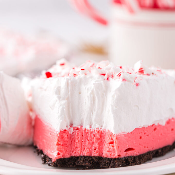 up close view of layered peppermint pie with a fork bite taken out of it. candy canes in the background