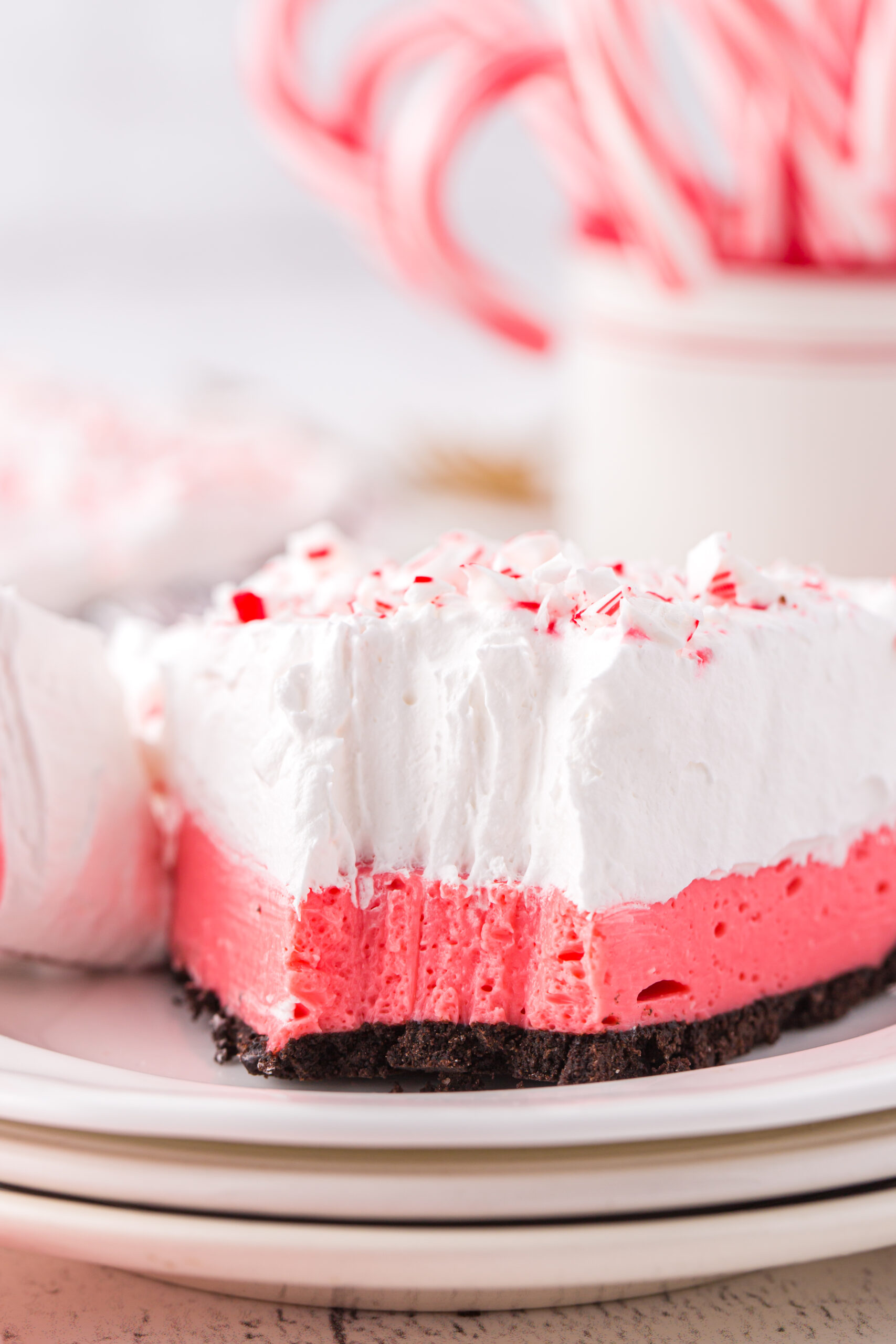 up close view of layered peppermint pie with a fork bite taken out of it. candy canes in the background