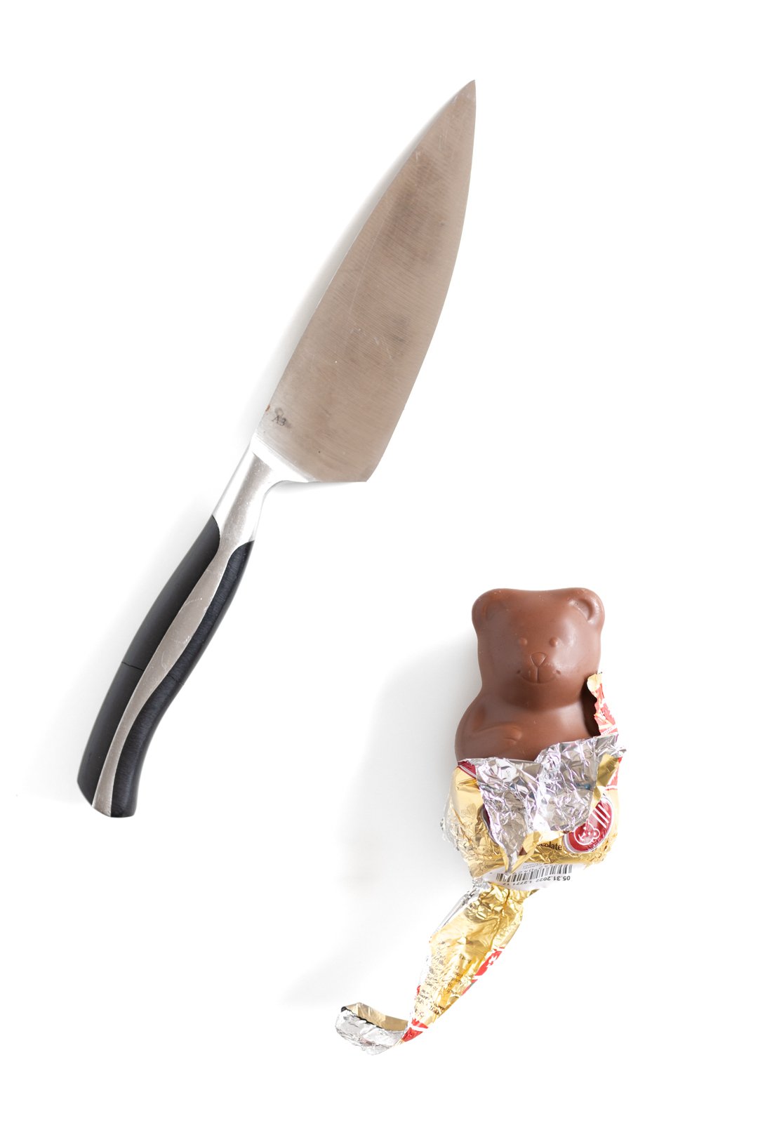 a half unwrapped chocolate teddy bear next to a knife to indicate the action of cutting