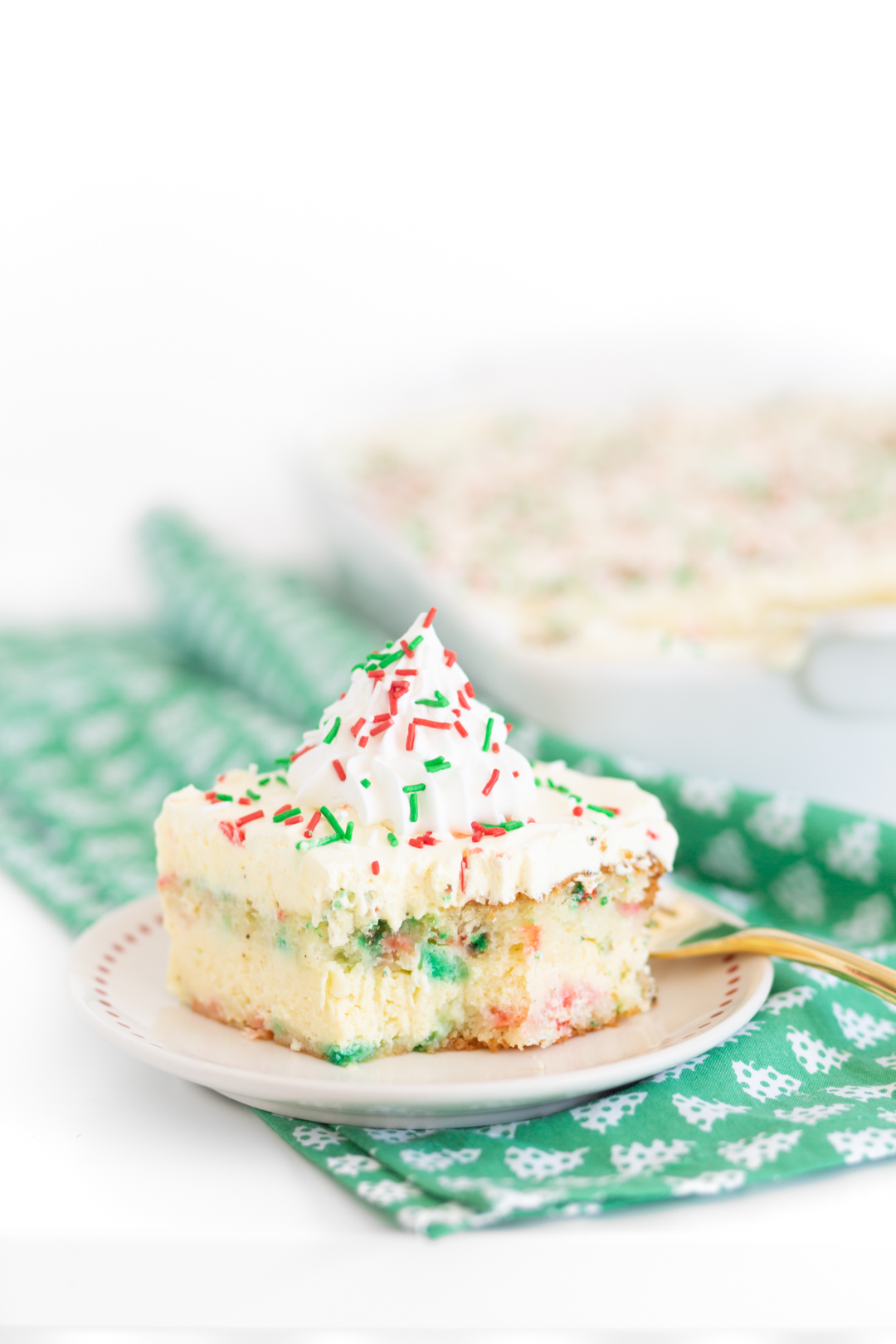 slice of pretty holiday layer cake on a small plate served in front of cake in casserole dish behind it.