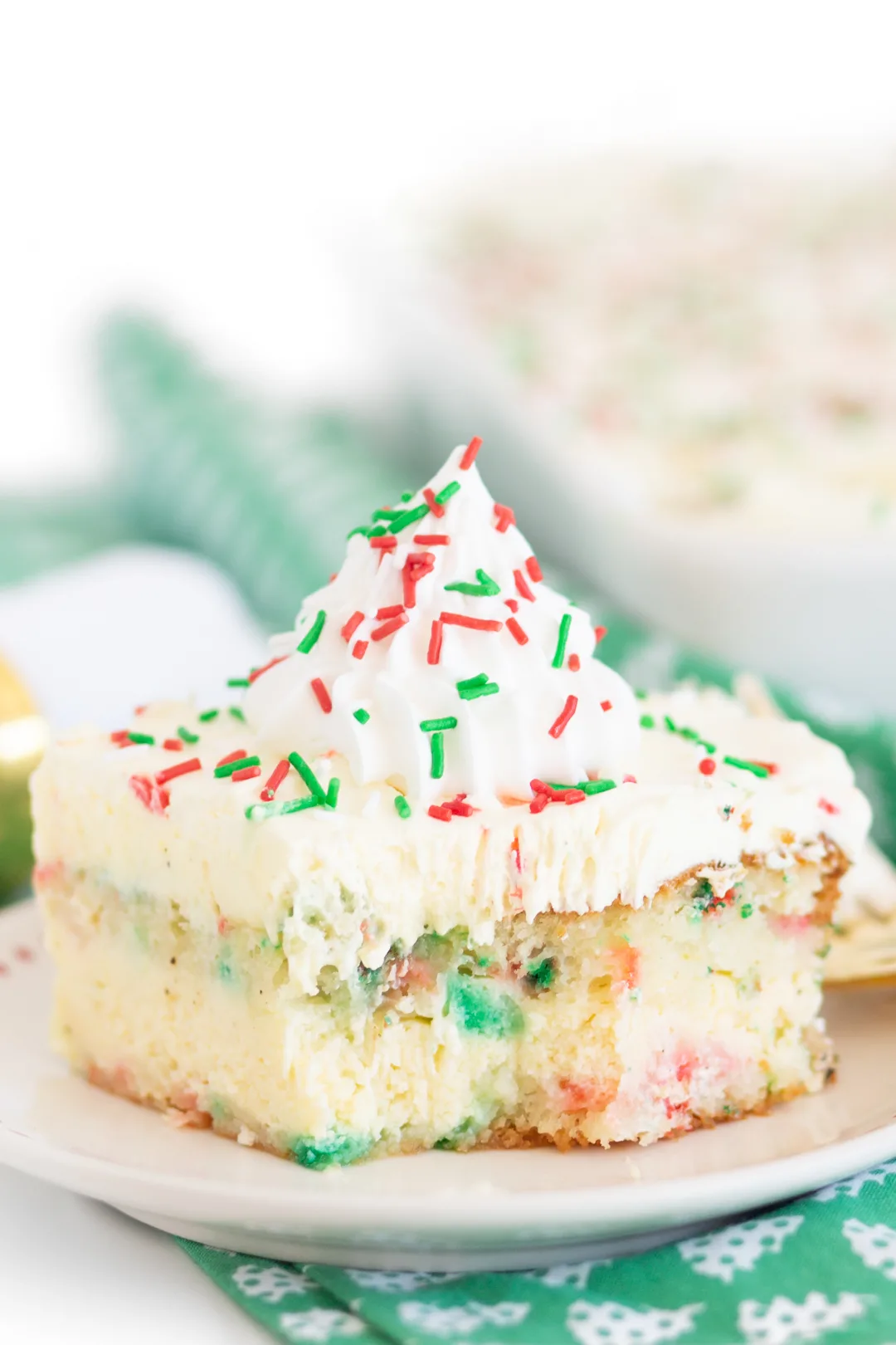 close up of chrismtas cake to showcase the three layers. topped with red and green sprinkles and a pretty dollop of whipped cream