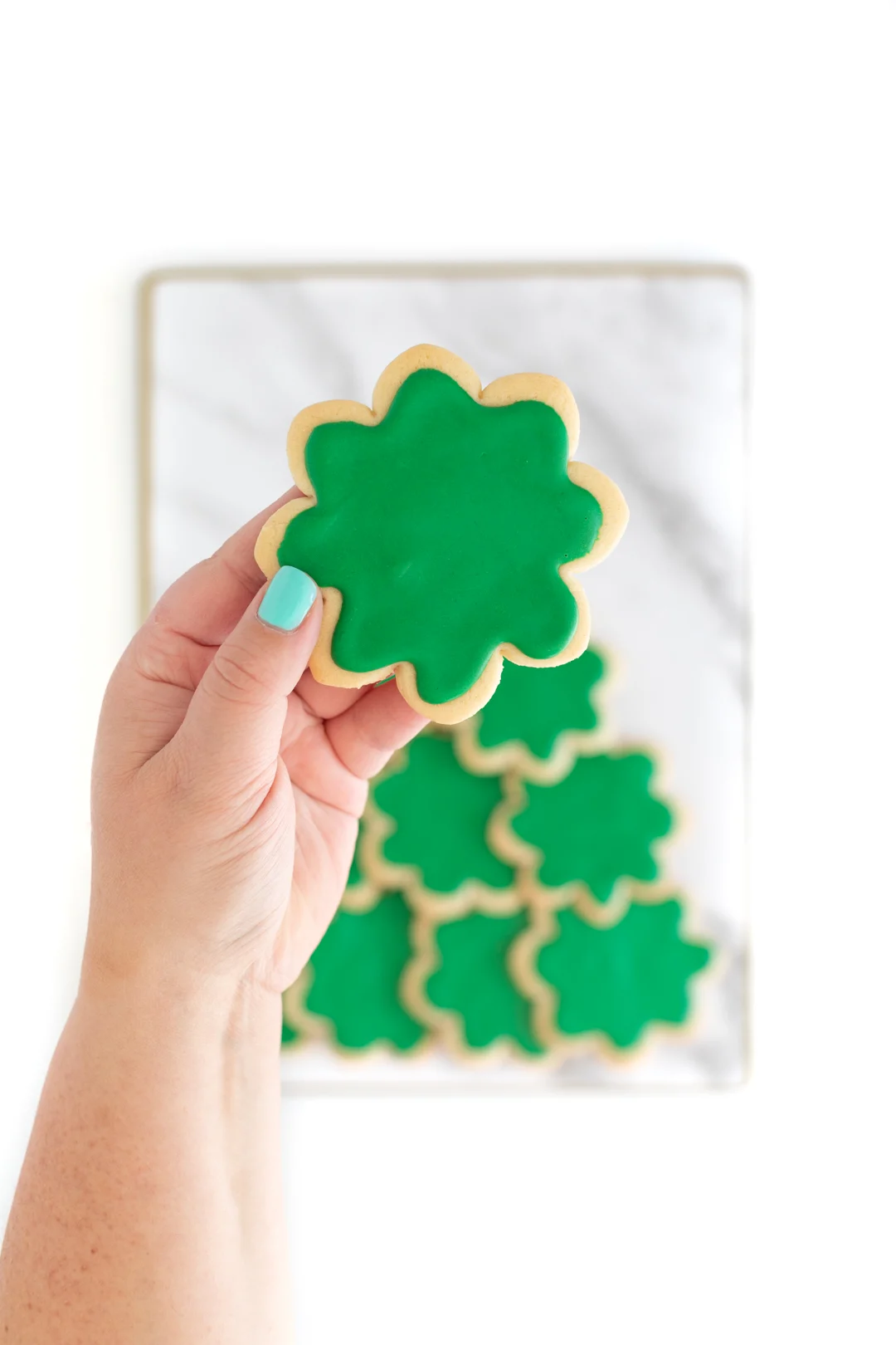 overhead photo of a woman 's hand holding a green frosted flower shaped cookie