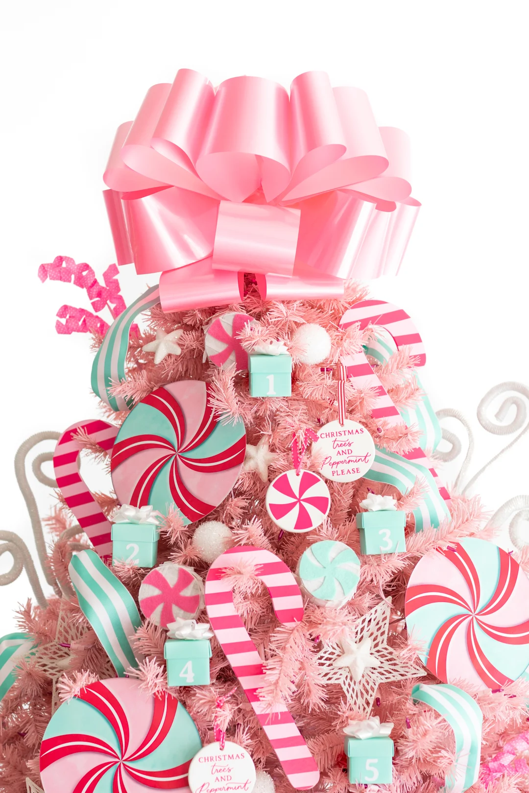 upper half of a decorated pink christmas tree with pink peppermint ornaments and decorations. Mini countdown gift boxes that are numbered for advent countdown.