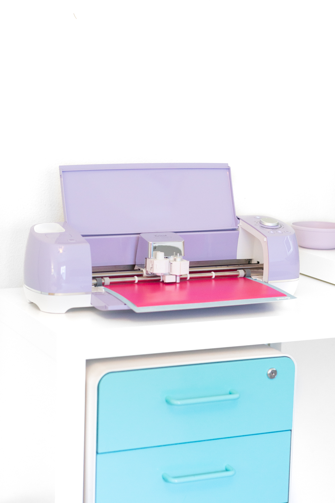 Purple Cricut Explore Air 2 loaded with cricut pink vinyl bing used on a white desk.