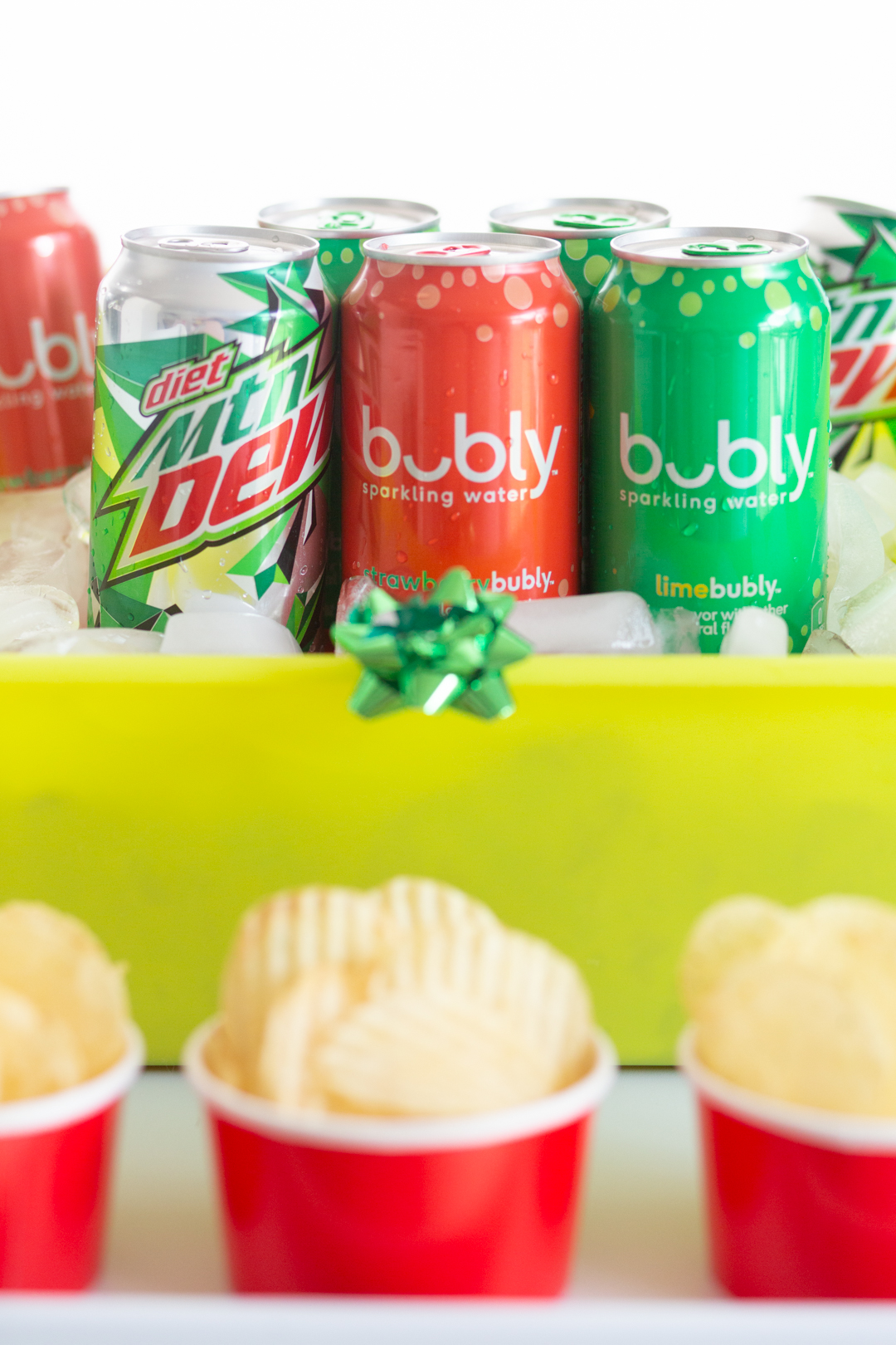 up close view of bubly drinks and diet mountain dew in a light green tub with ice. chips in individual snack ups in front of the cooler.