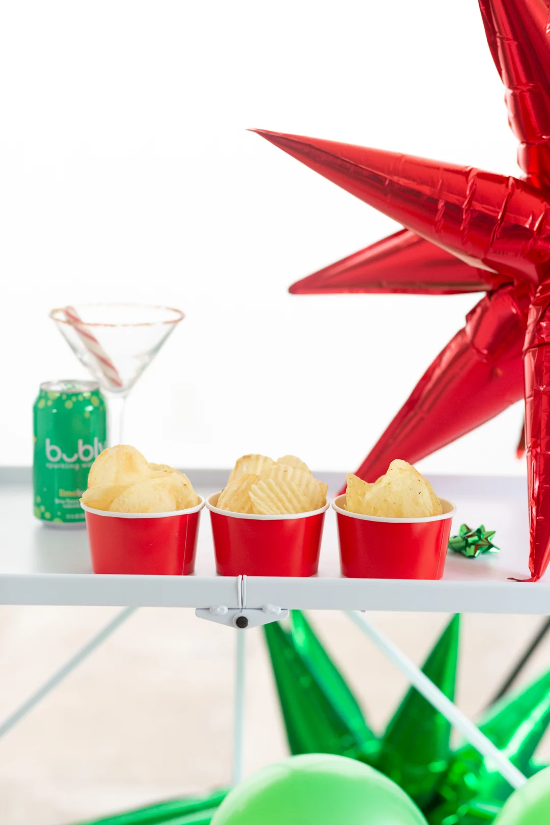 chips being served in snack cups on a bar cart decorated with large red and green star foil balloons