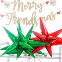 merry friends banner hung above a white bar cart with large foil star balloons that are red and green