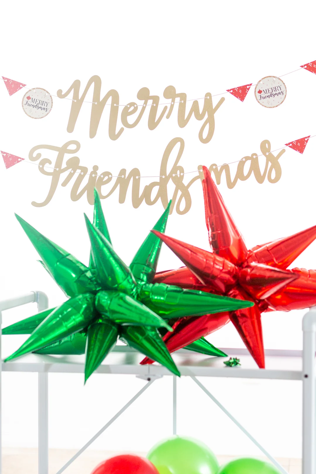 merry friends banner hung above a white bar cart with large foil star balloons that are red and green