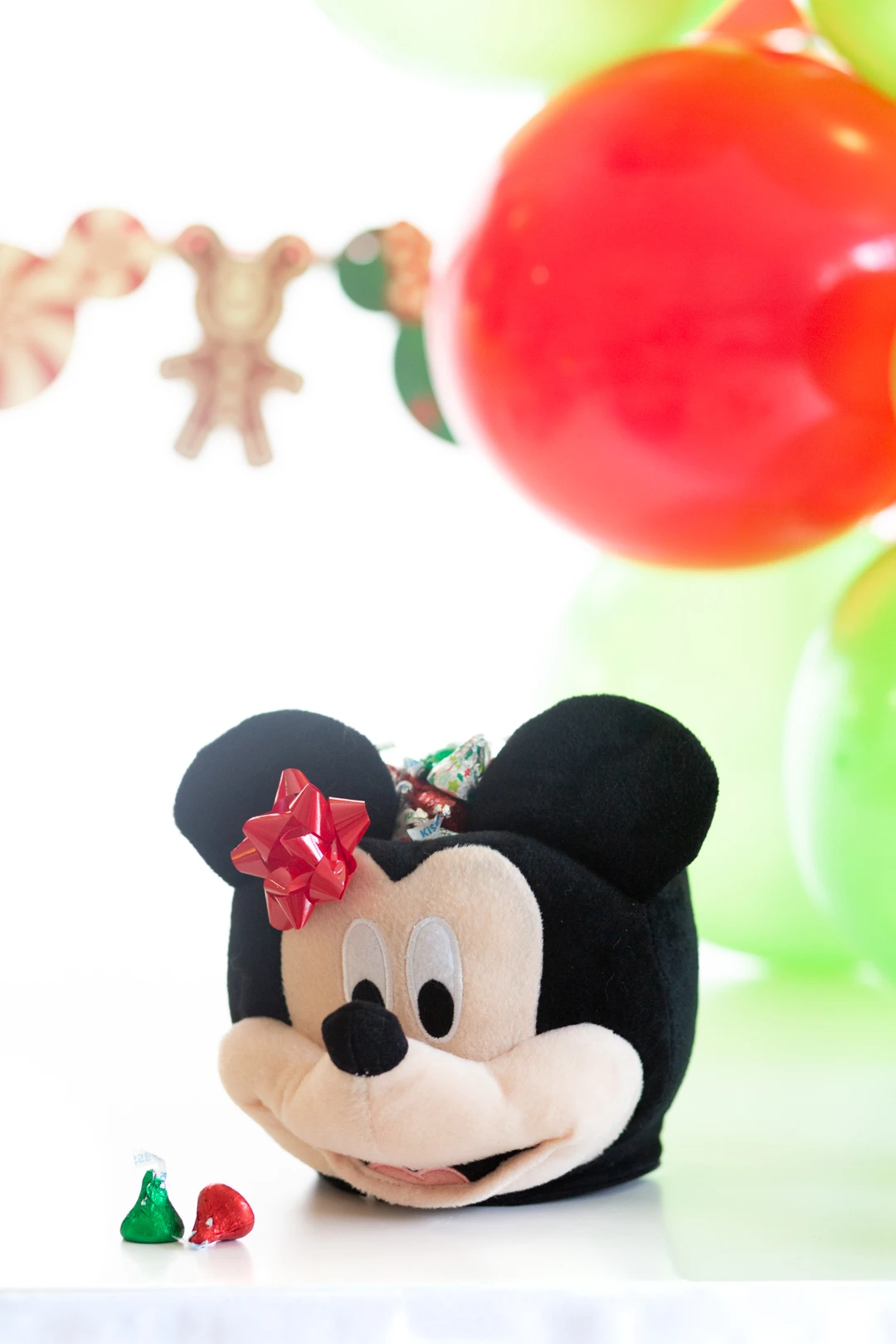 mickey mouse halloween treat bucket shaped like mickey mouse head being used to celebrate christmas. small gif bow on top to decorate and filled with christmas themed hershey's kisses