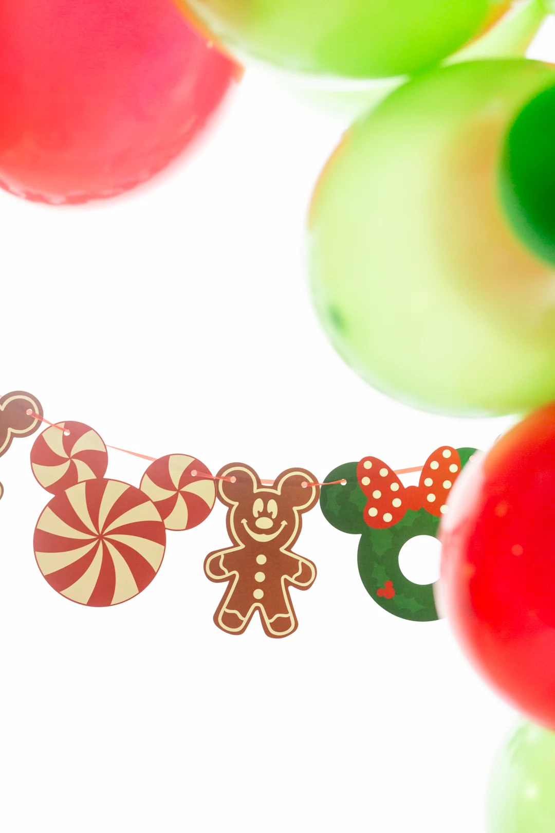christmas themed mickey mouse party banner surrounded by red and green balloons. mickey mouse gingerbread man, mickey shaped peppermint, mickey shaped wreath decorations on the banner