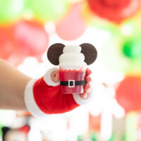 santa belt jello cups with oreo cookie ears to look like mickey mouse. single cup being held by woman with fingerless santa glove