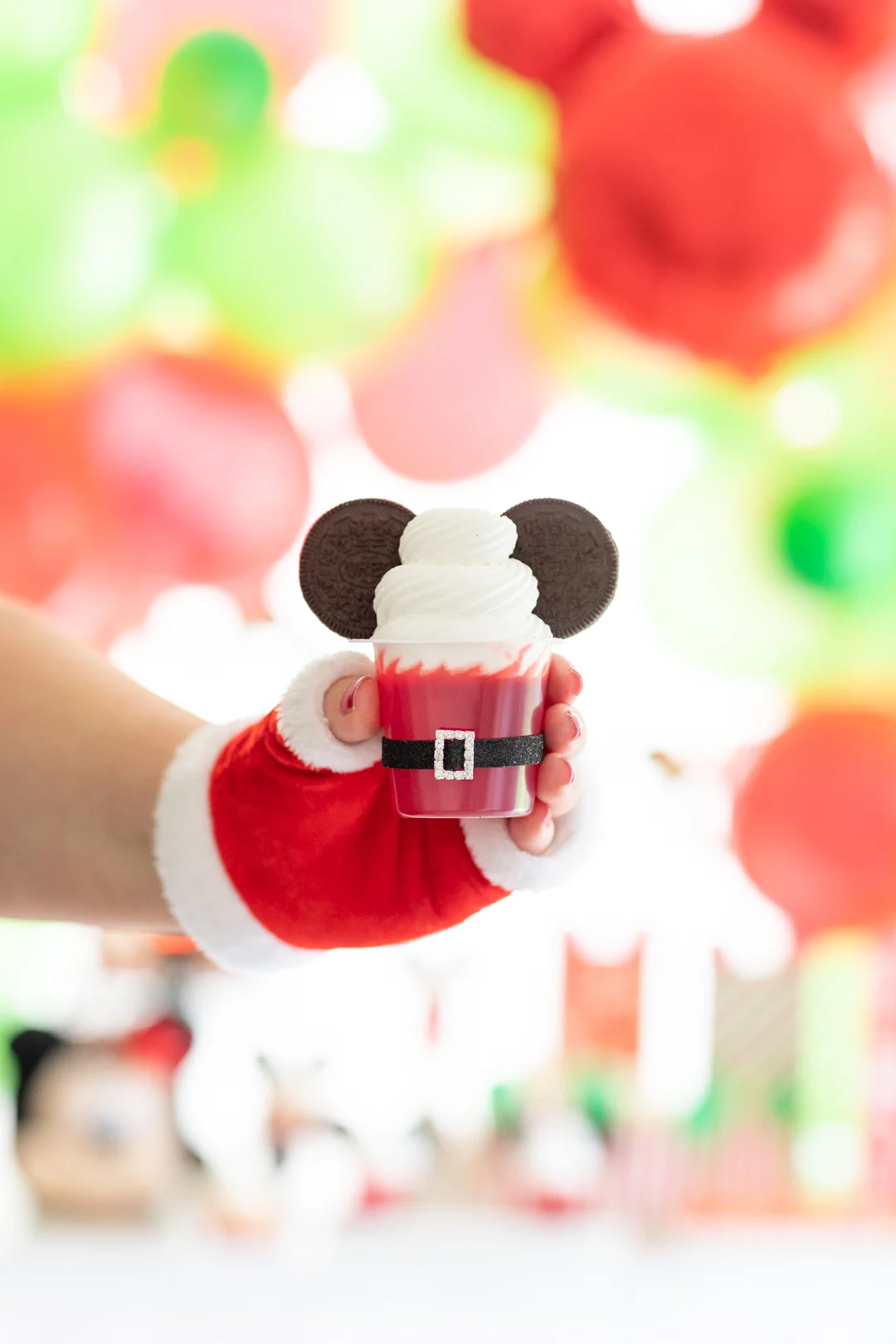 santa belt jello cups with oreo cookie ears to look like mickey mouse. single cup being held by woman with fingerless santa glove
