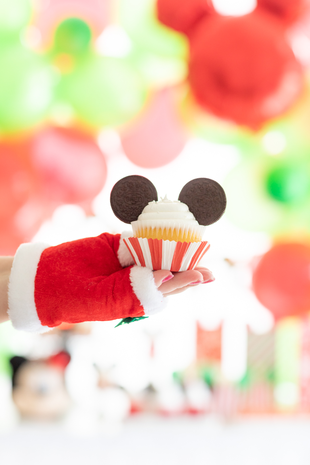 woman with fingerless santa gloves holding a christmas themed mickey mouse cupcake