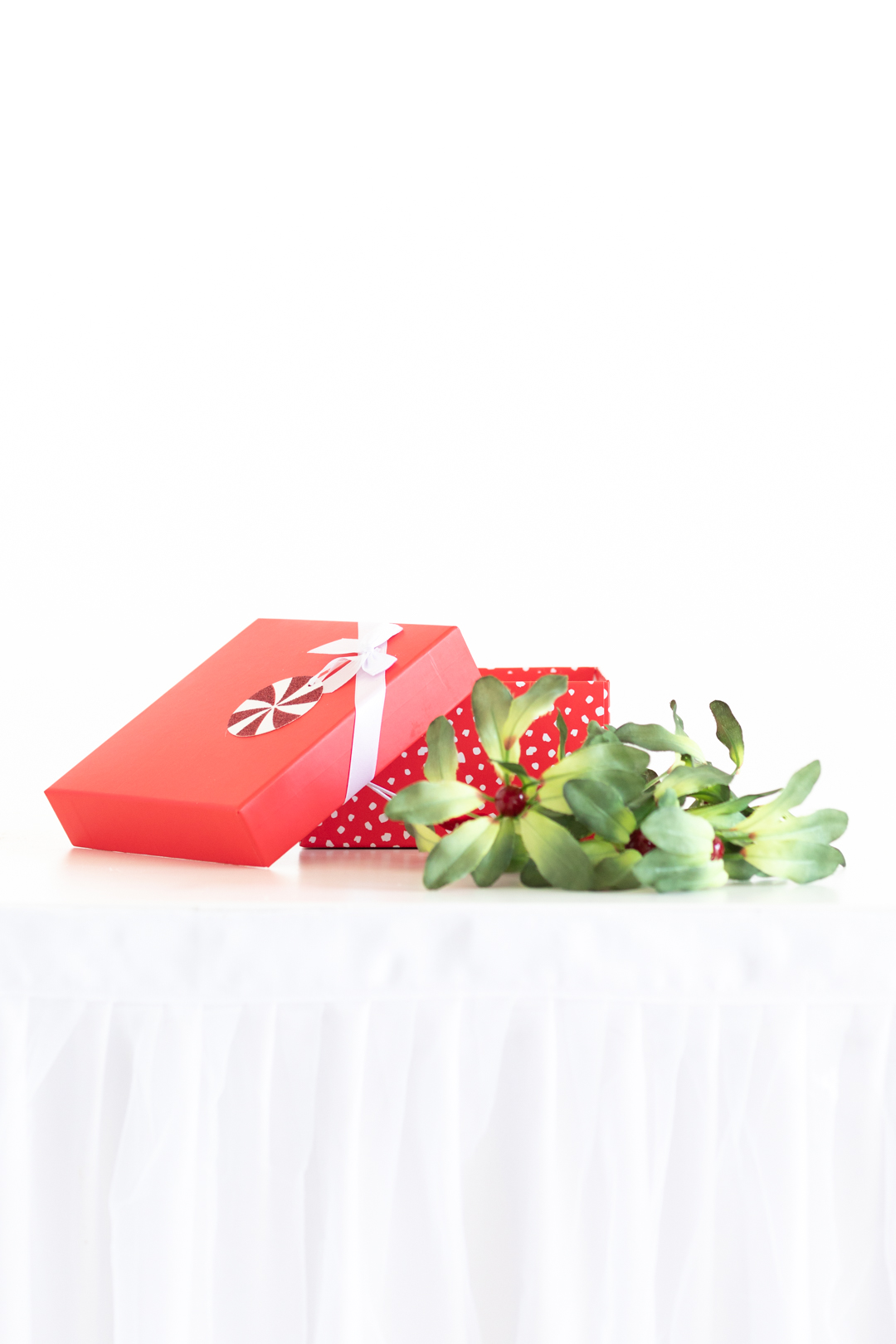 empty red gift box and mistletoe set out on a white table