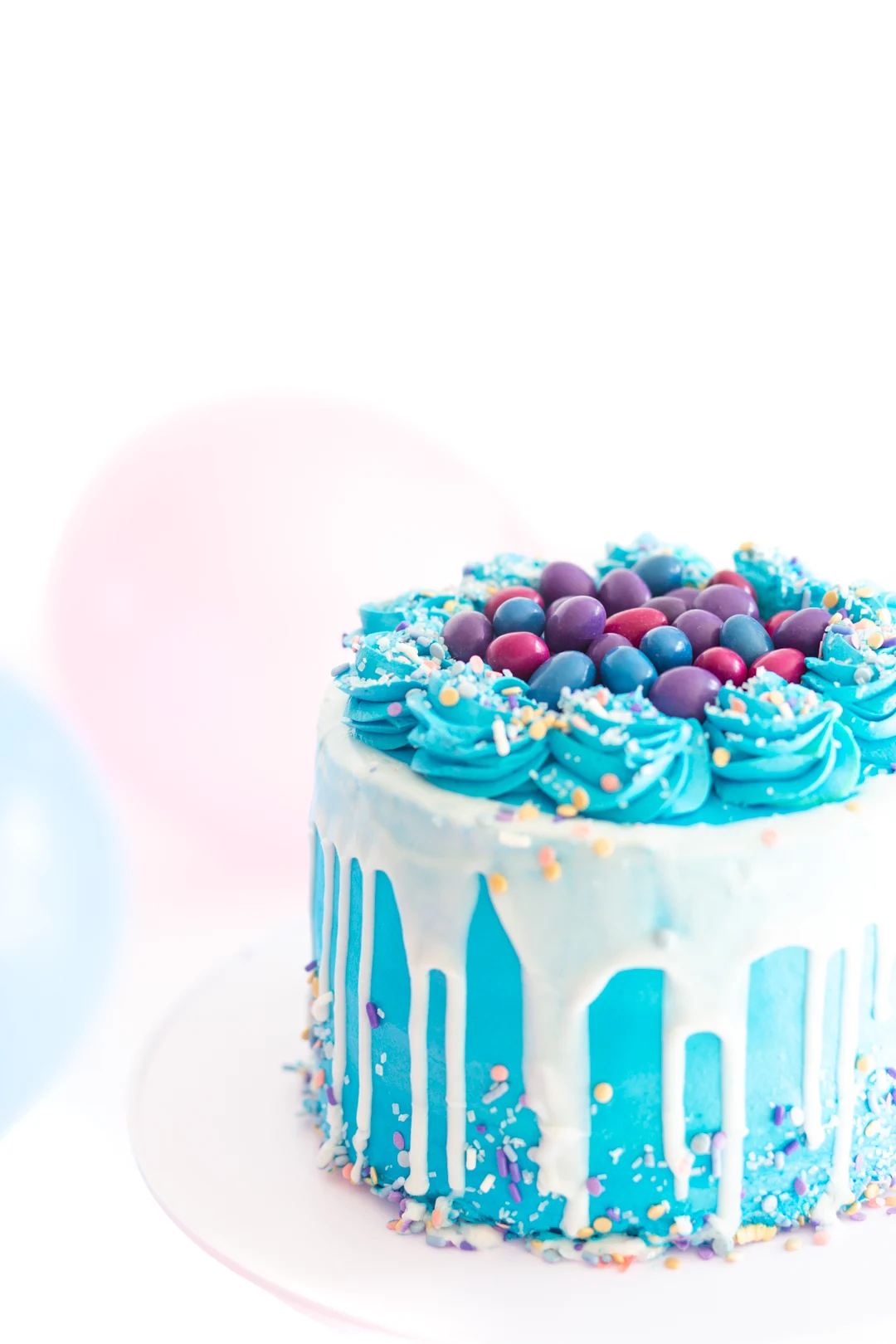 pretty blue cake with white icing drip. Topped with pretty swirls of blue frosting designs and finished with pretty candy coated candies that are purple, pink and blue.