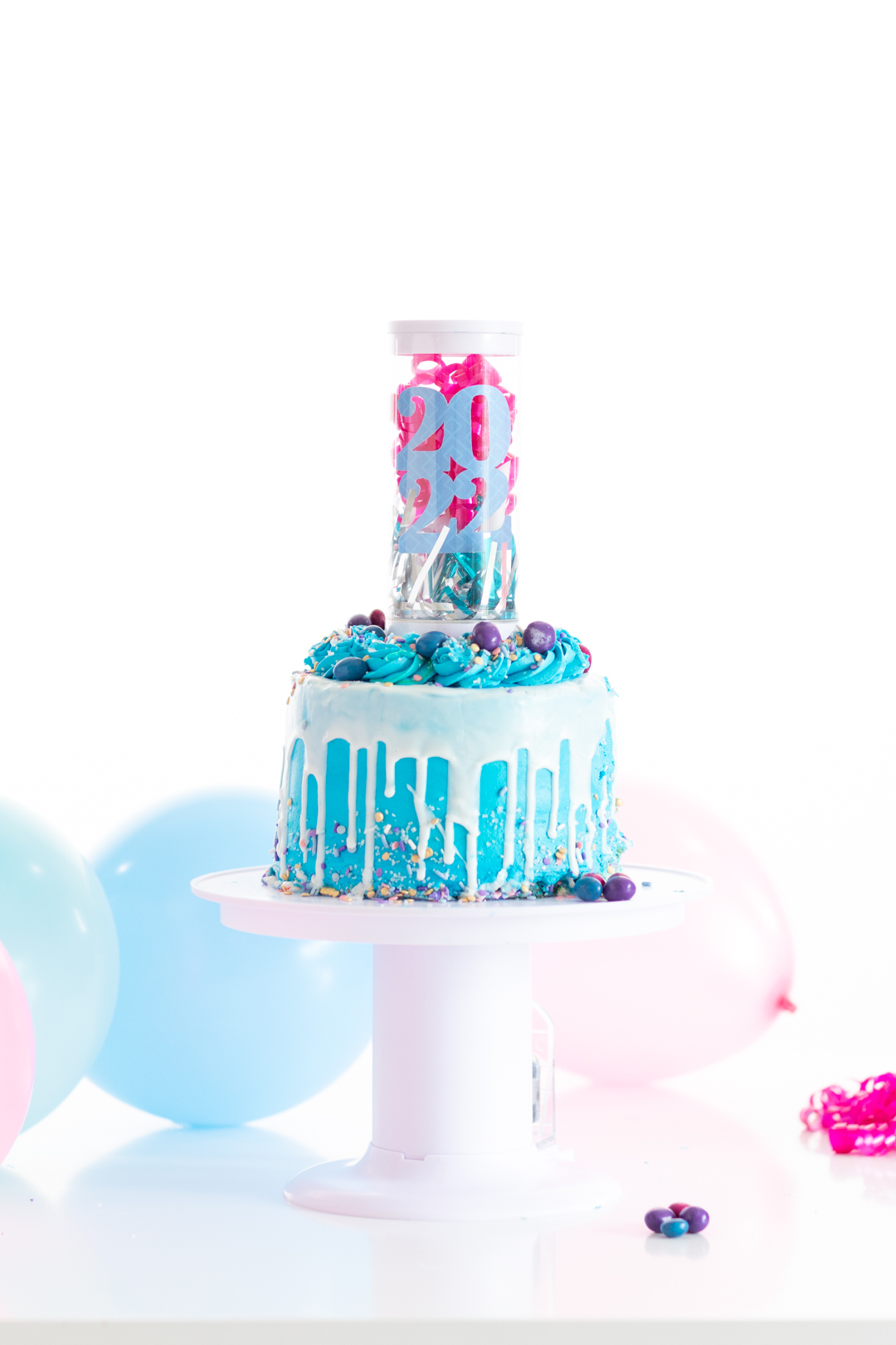small cake with a 2022 surprise popped out of the center. A clear tube with 2022 decoration, party blowers and pink curly gift bow