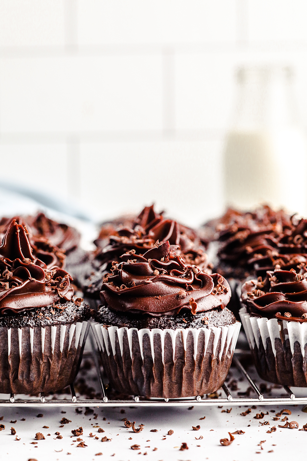 batch of chocolate cupcakes with chocolate frosting resting on kitchen counter. blurred single glass bottle of milk in background