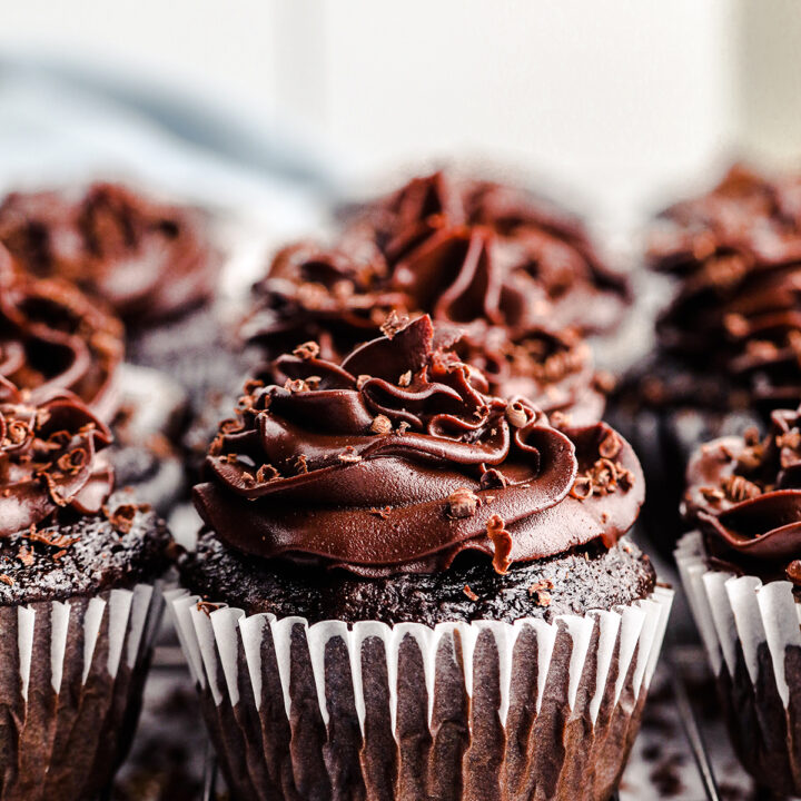 up close view of a batch of chocolate cupcakes with chocolate frosting and chocolate shavings on top.