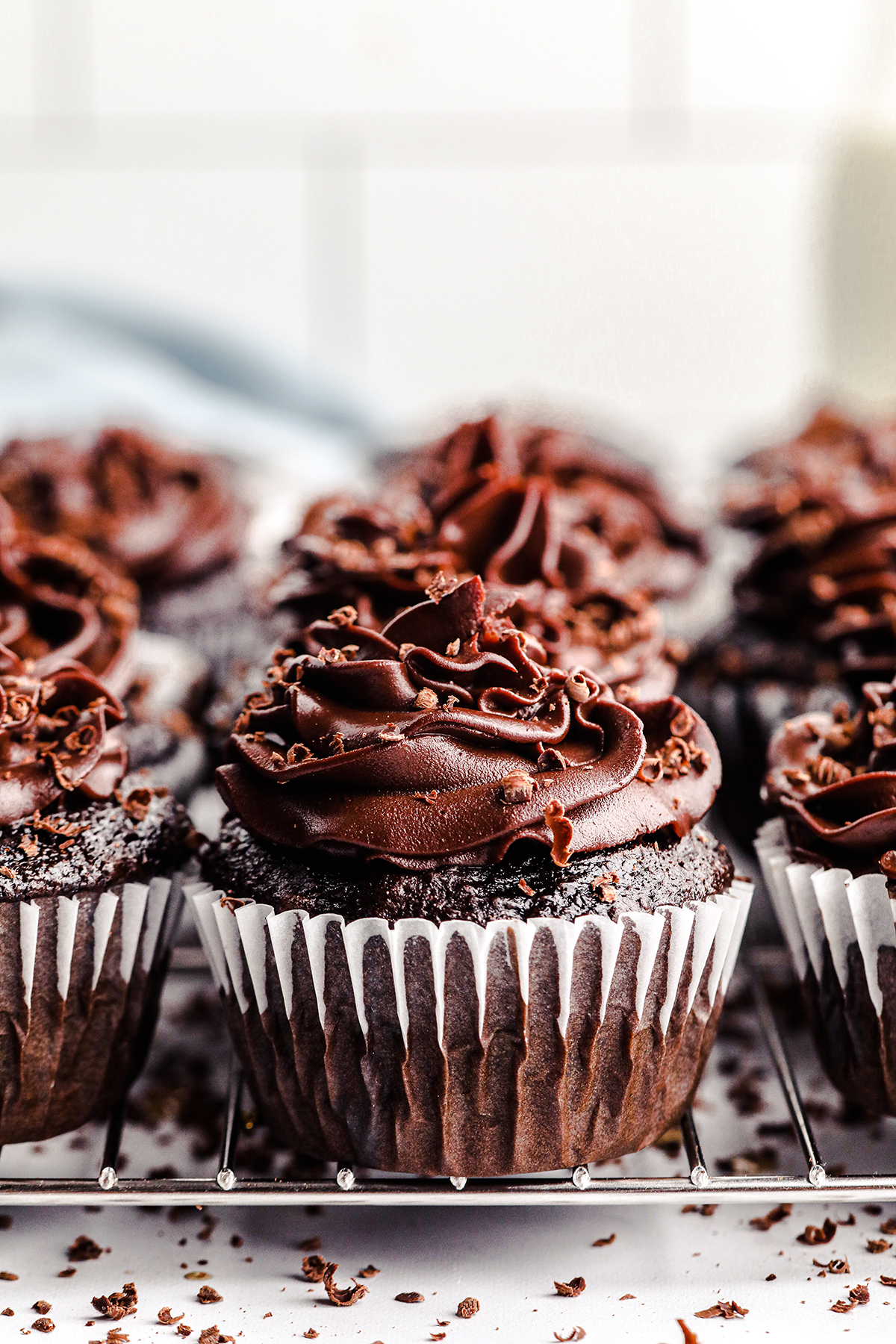 up close view of a batch of chocolate cupcakes with chocolate frosting and chocolate shavings on top.