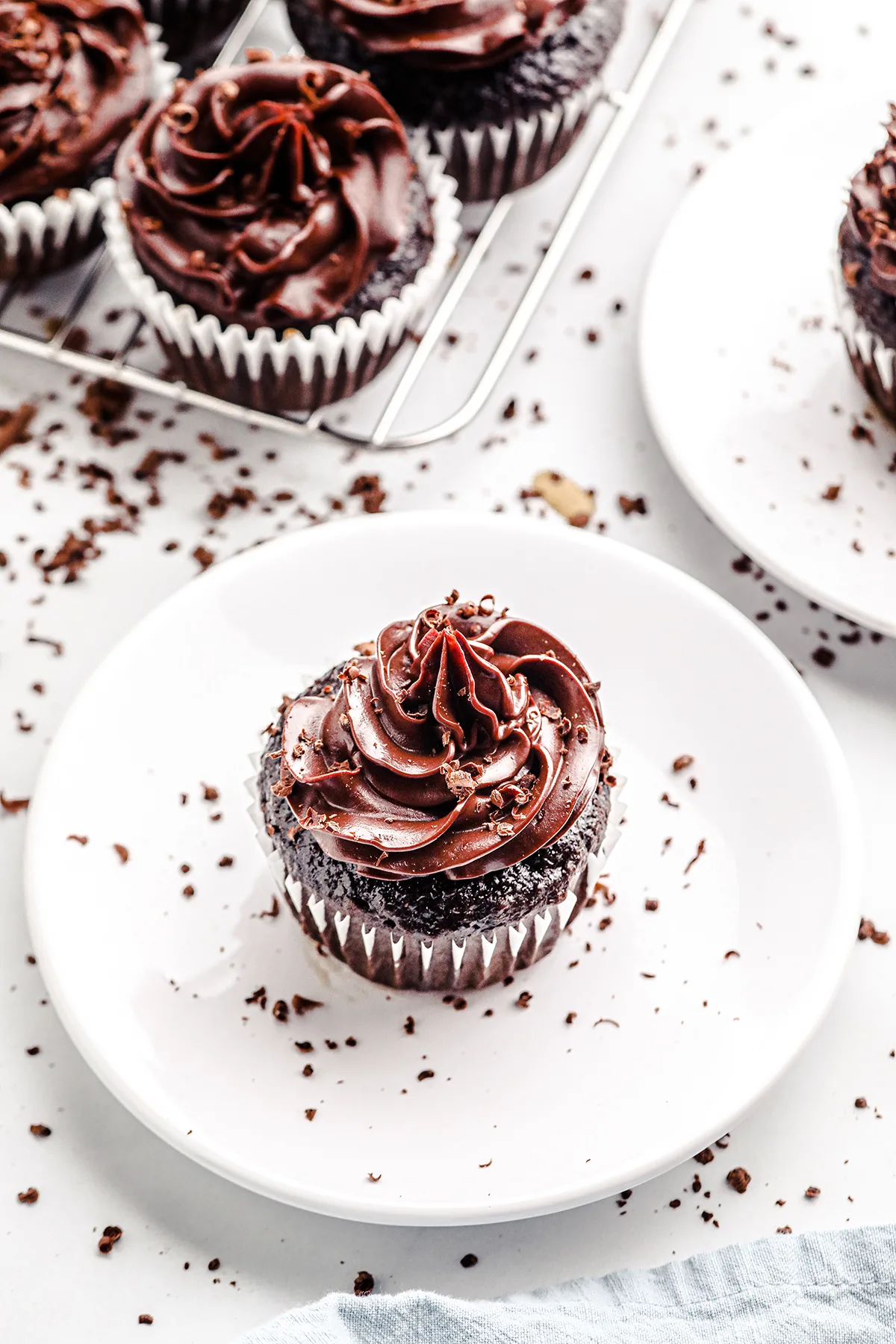 chocolate frosted cupcake being served on a small white plate and sprinkled with small chocolate shavings