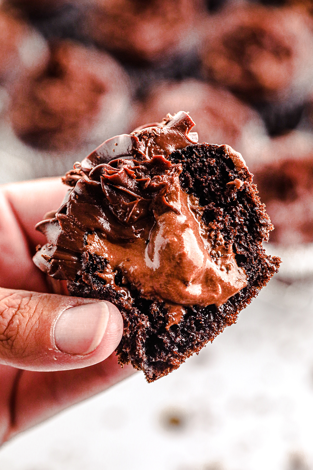 woman holding a halved cupcake with chocolate mousse oozing out of it.