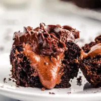 halved chocolate cupcake with chocolate frosting with a chocolate filling oozing out of the center on a small white dish.