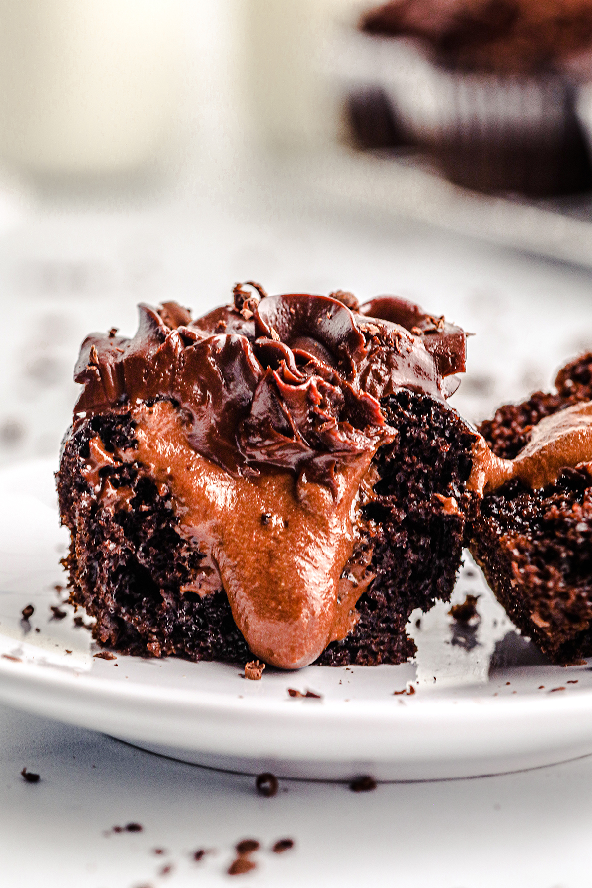 halved chocolate cupcake with chocolate frosting with a chocolate filling oozing out of the center on a small white dish.