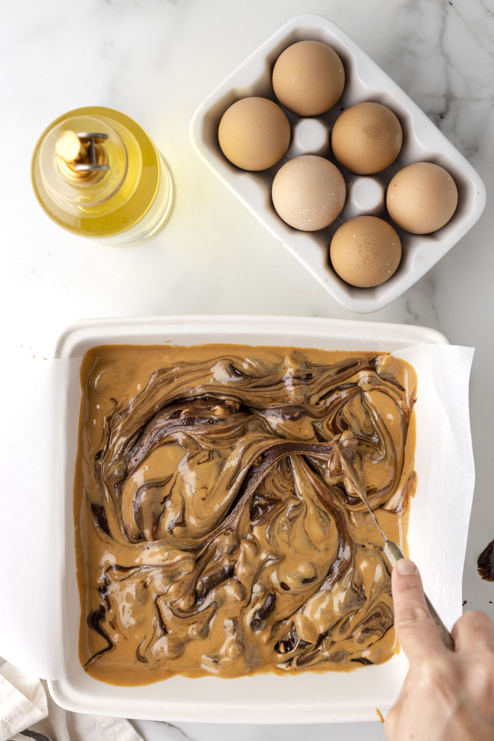 baking dish with swirled peanut butter brownie mix batter. eggs and oil nearby.